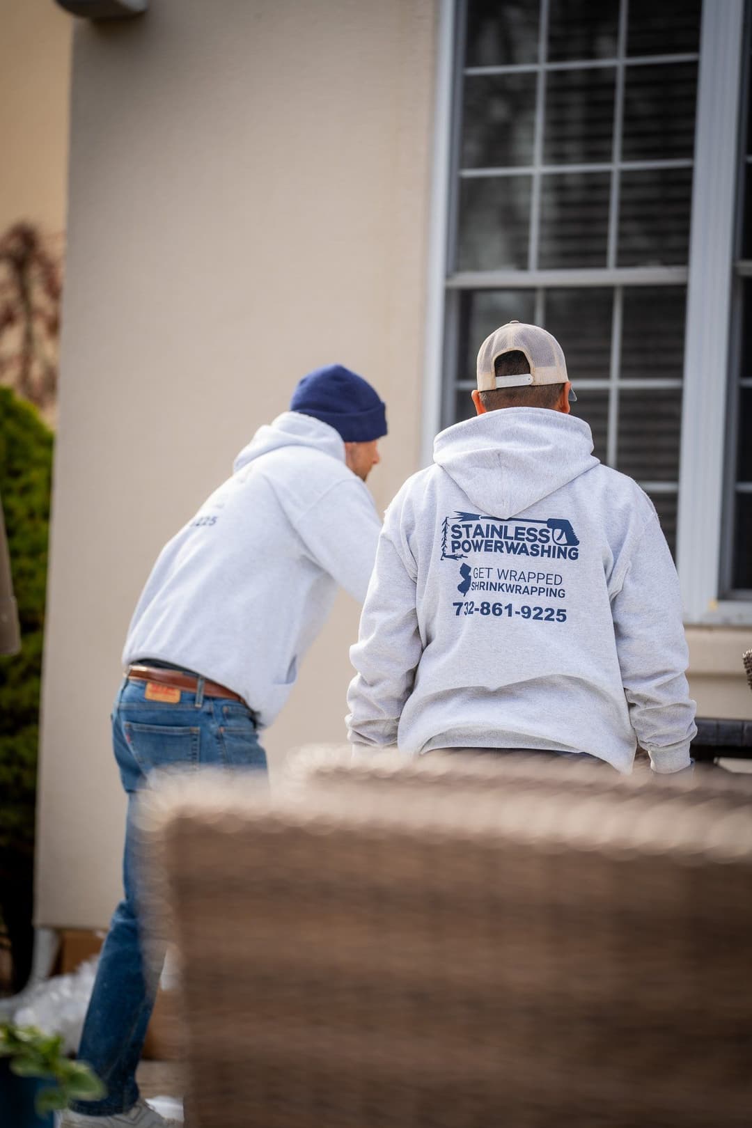 Two workers in hoodies from Stainless Steel Powerwashing preparing for a job outside a home.