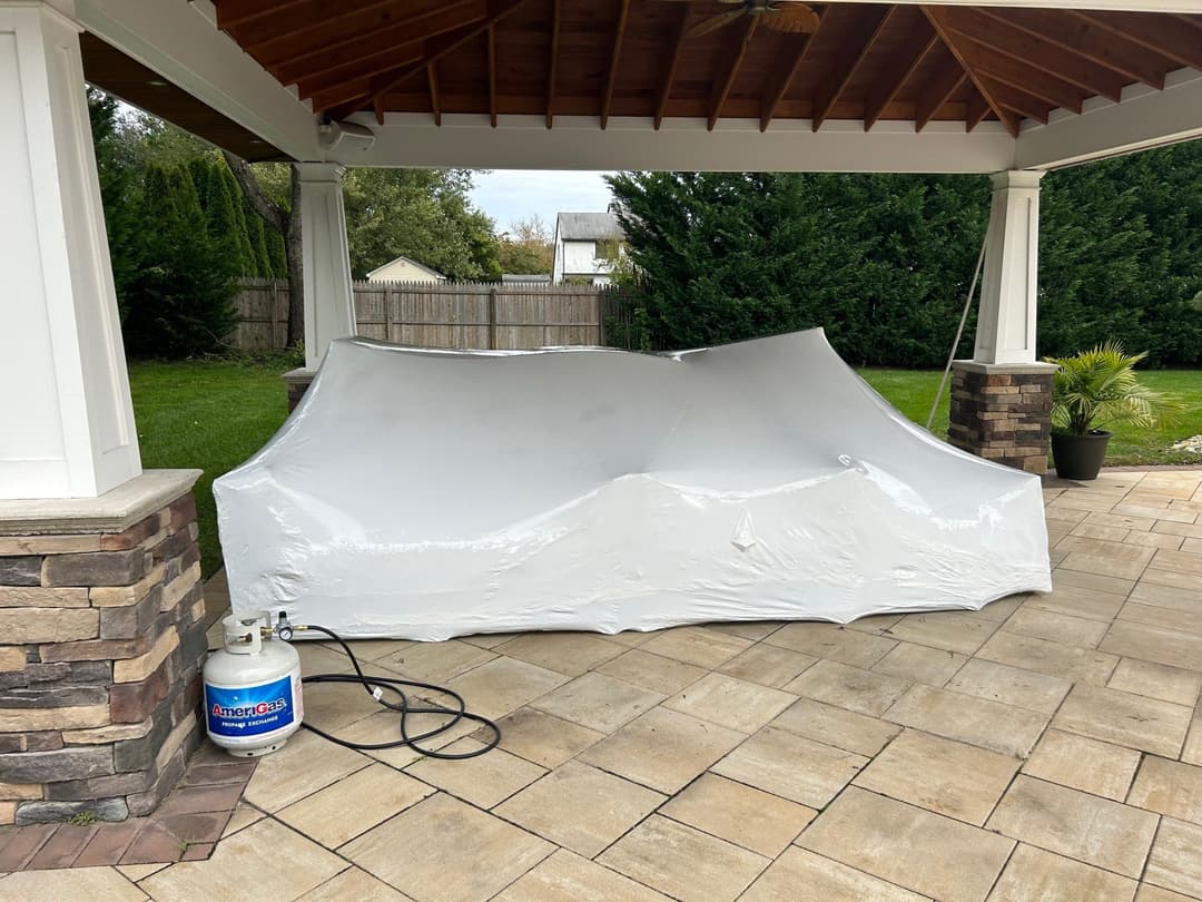 Outdoor covered furniture on a patio with a propane tank nearby.
