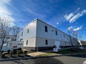 Exterior view of a large white industrial building with blue sky and clouds.