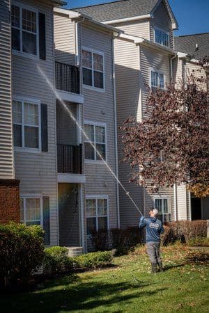 Person using a pressure washer to clean the exterior of an apartment building.