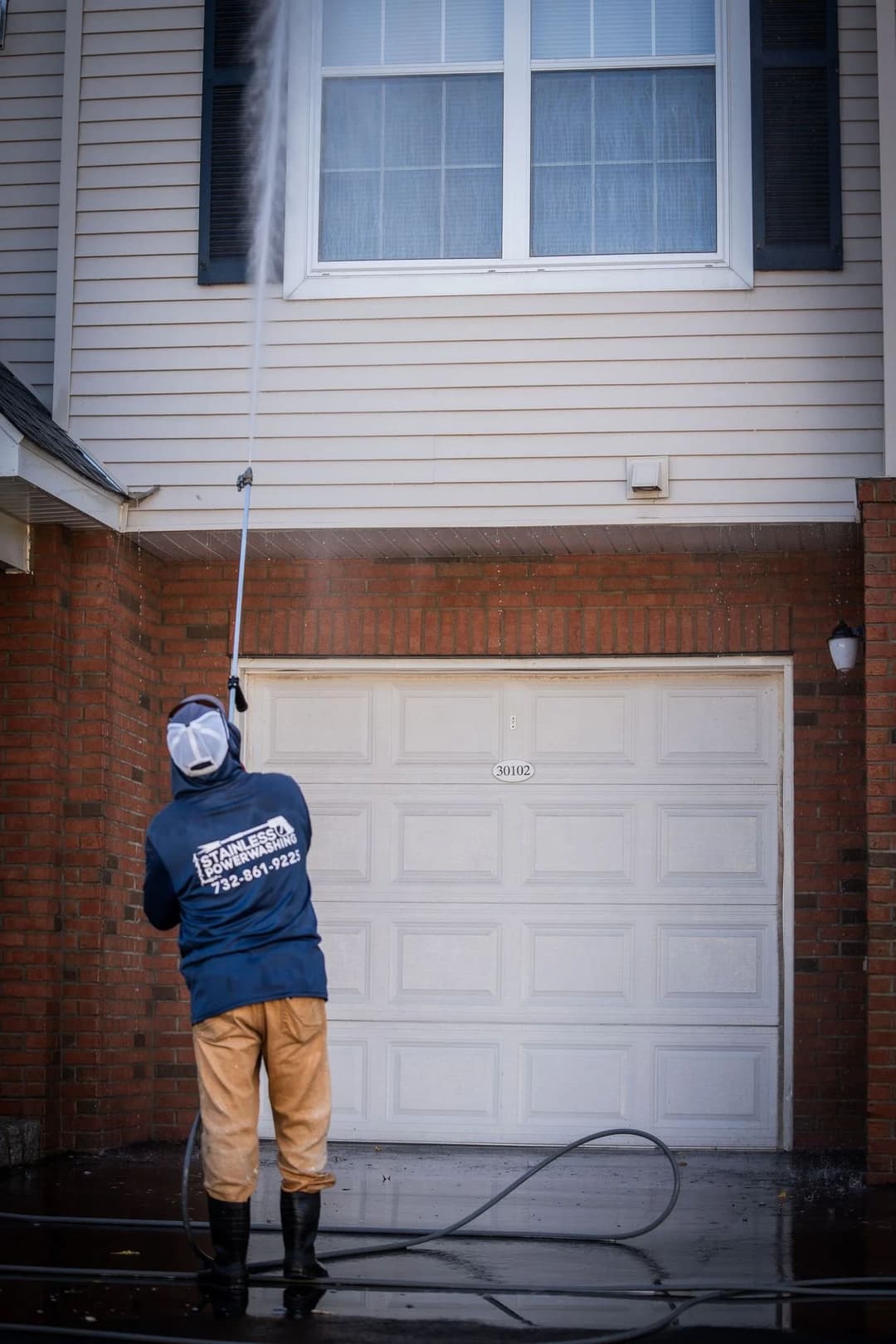 Person pressure washing a home's exterior, showcasing a clean garage and window area.