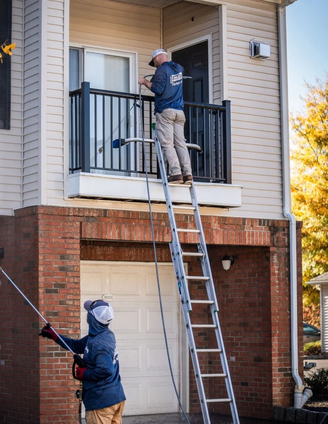 Two workers using a ladder to clean a balcony, showcasing home maintenance services.