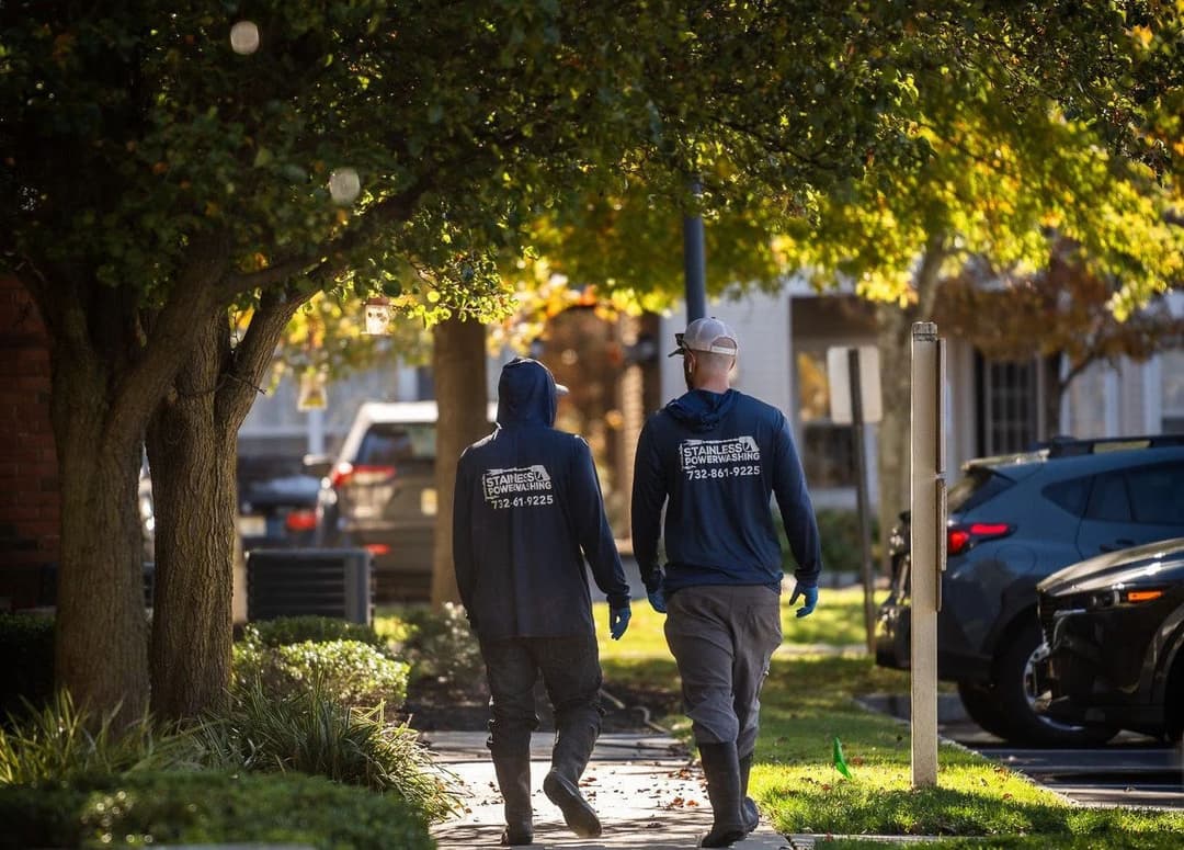 Two workers in hooded sweatshirts walking along a tree-lined sidewalk, promoting teamwork.