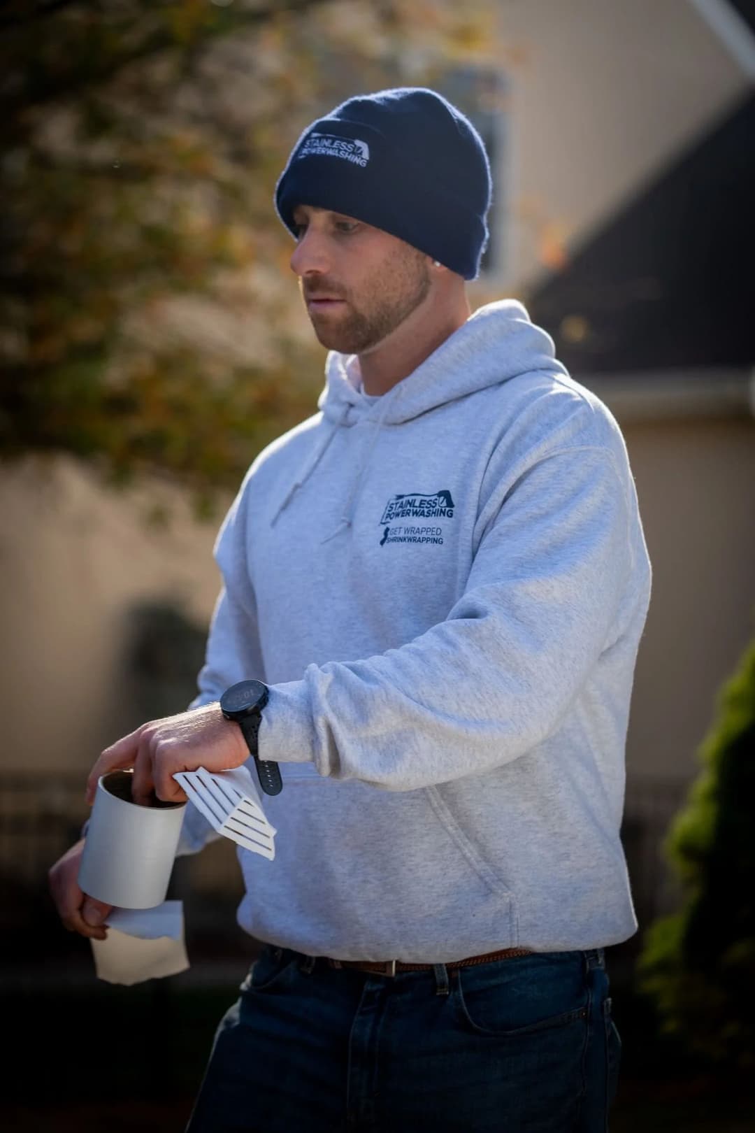 Man in a hoodie and beanie holding a cup outdoors on a sunny day.