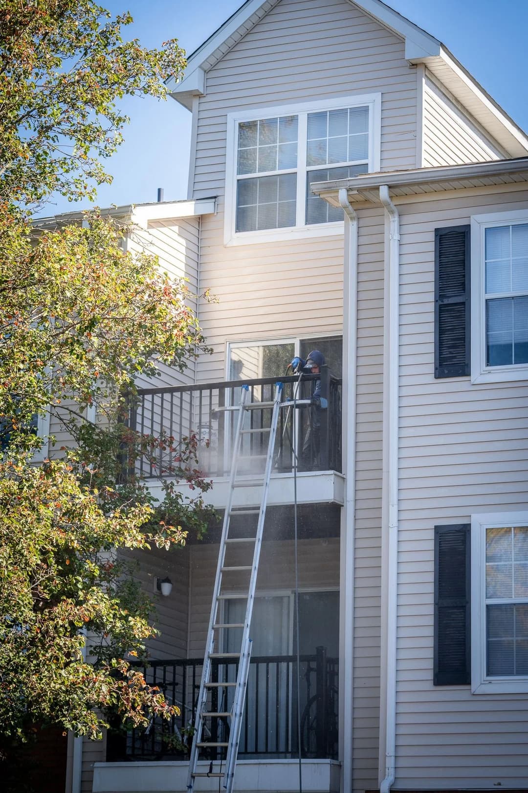 Person cleaning a balcony of a multi-story apartment building using a ladder and pressure washer.
