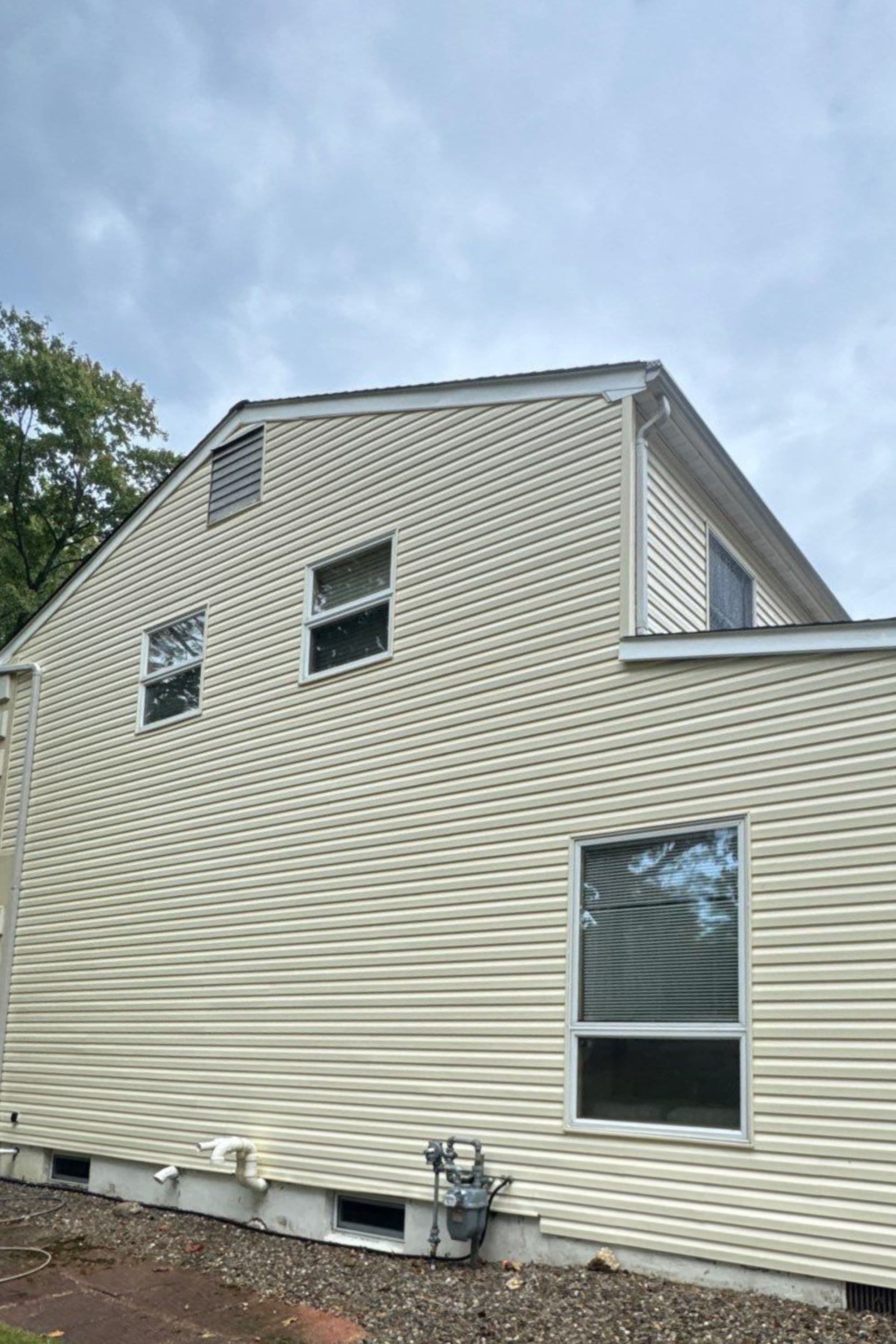Side view of a residential home with beige siding and multiple windows under a cloudy sky.