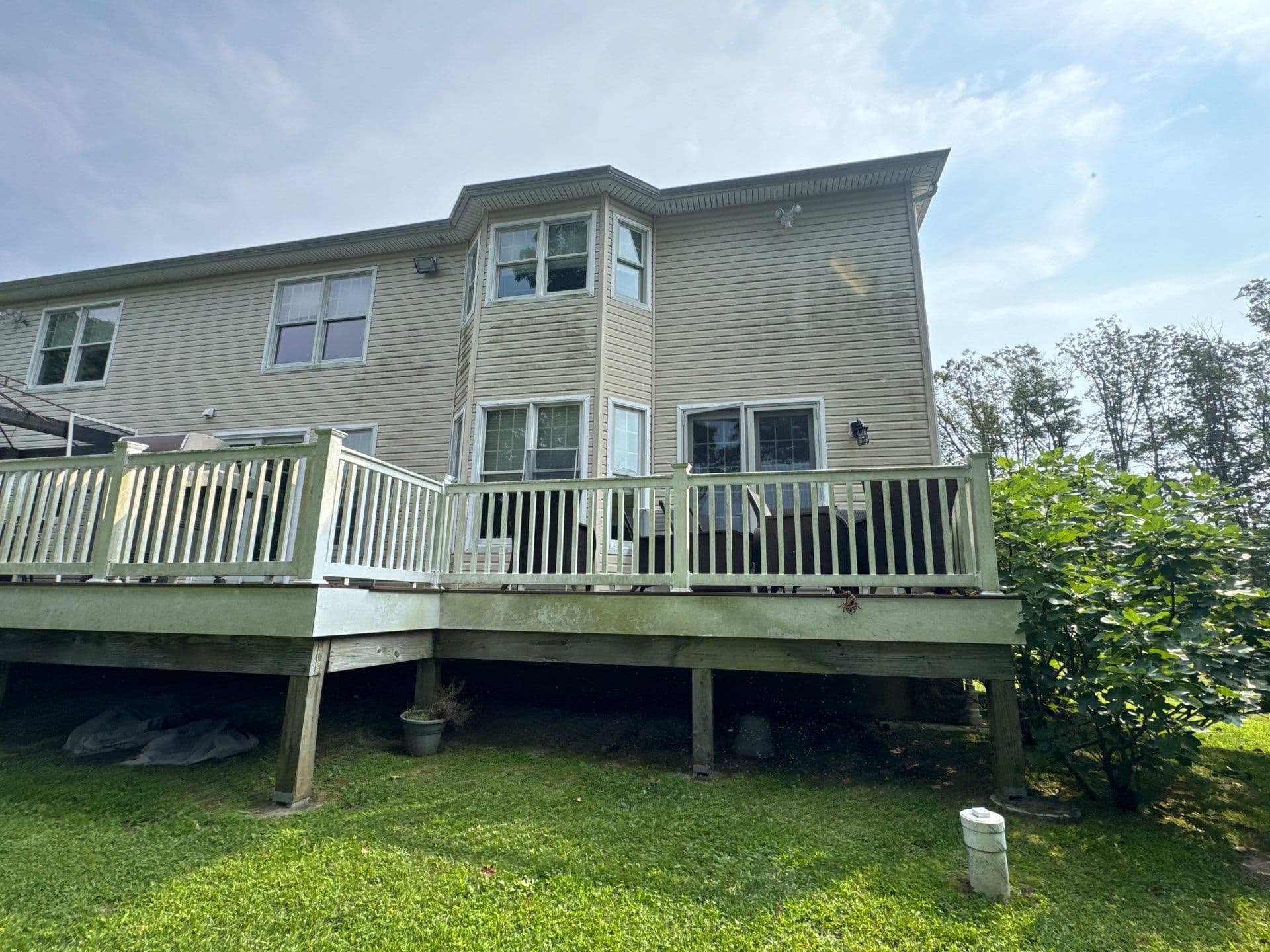 Two-story house exterior with deck, surrounded by greenery on a sunny day.