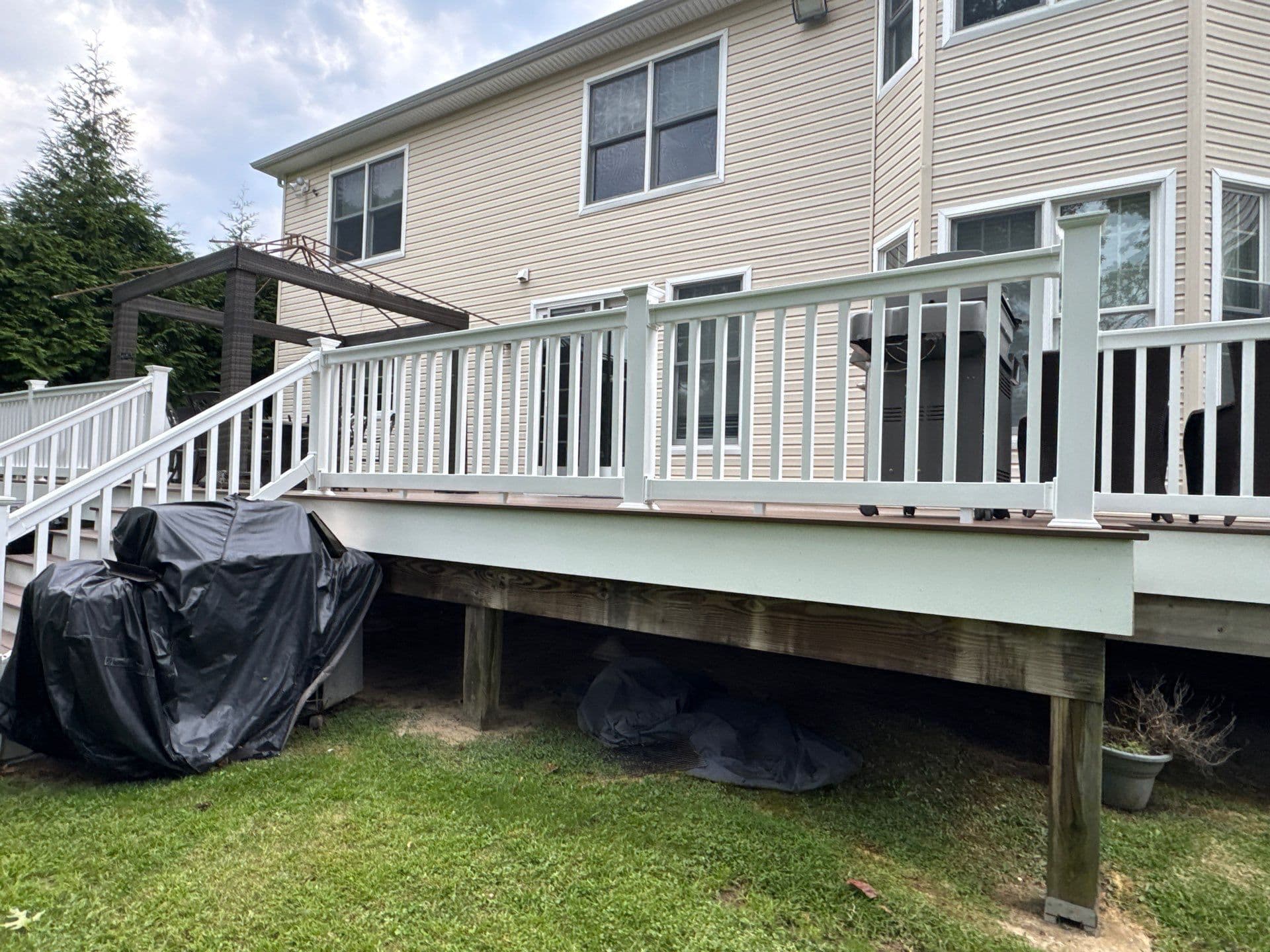 Modern backyard deck with white railing, grill, and covered furniture. Comfortable outdoor space.