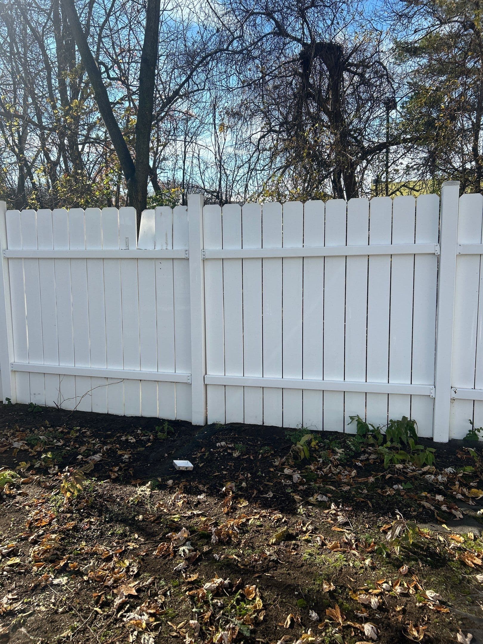 White wooden fence in a yard surrounded by autumn leaves and trees.